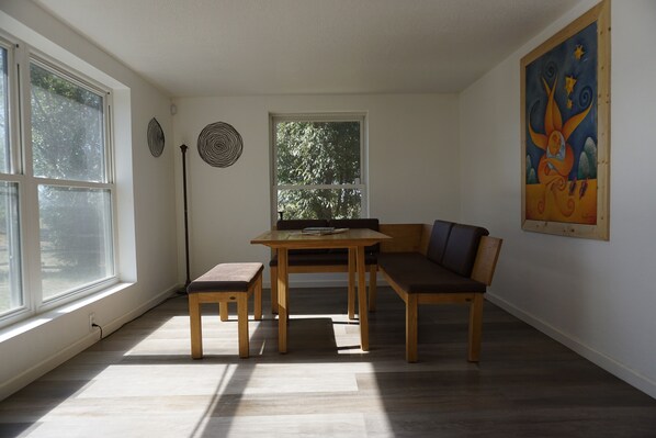 Une pièce avec une grande fenêtre, une table avec des chaises, un banc et un tableau accroché au mur.