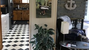 Una sala de estar con piso a cuadros blanco y negro, una planta en maceta, un sofá, una mesa de centro y una pared con un letrero que dice 'Love' y una decoración de ancla.
