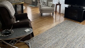 Una sala de estar con chimenea de piedra, televisor, sillón gris y alfombra estampada.