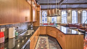 Eine moderne Küche mit Holzschränken, einer schwarzen Arbeitsplatte und einer großen Kochinsel. Es gibt eine Spüle, einen Herd und ein Fenster, das für natürliches Licht sorgt.