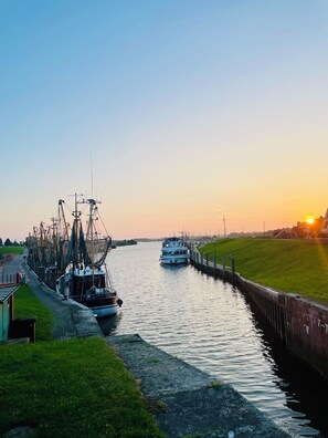 A canal with boats docked on the left, a grassy bank on the right, and a sunset in the background.