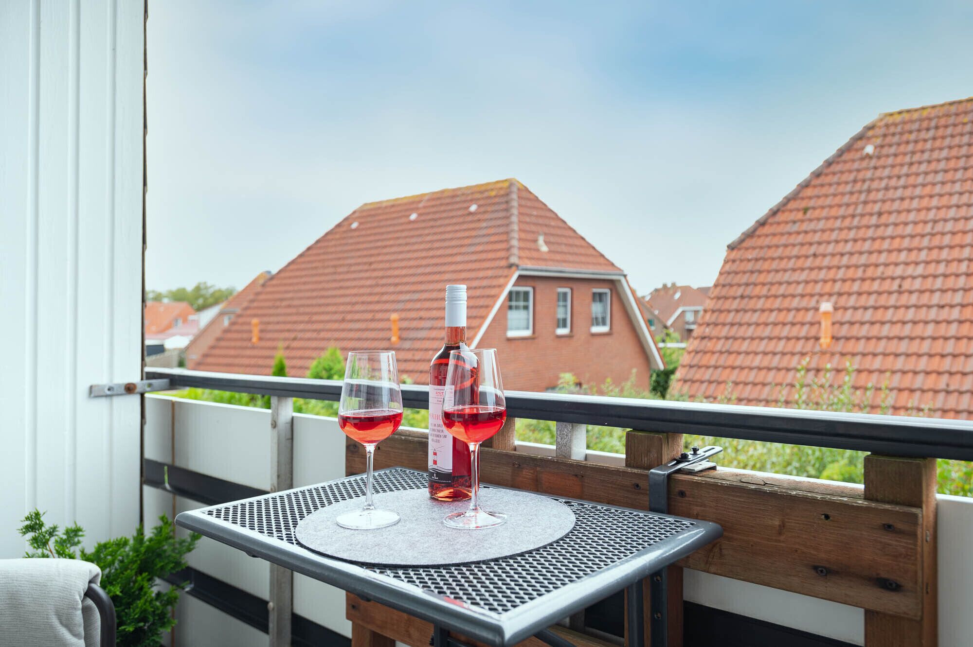 A balcony with a table, two wine glasses, and a bottle of wine.