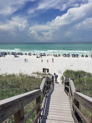 A wooden boardwalk leading to a sandy beach with umbrellas and lounge chairs.