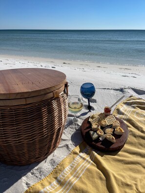 A beach setting with a wicker basket, a wooden drum, a glass of white wine, and a plate of pastries on a blanket. - You Want 30A, Stay on 30A! Salty Blonde @ Gulf Place steps from  deeded beach (Santa Rosa Beach)