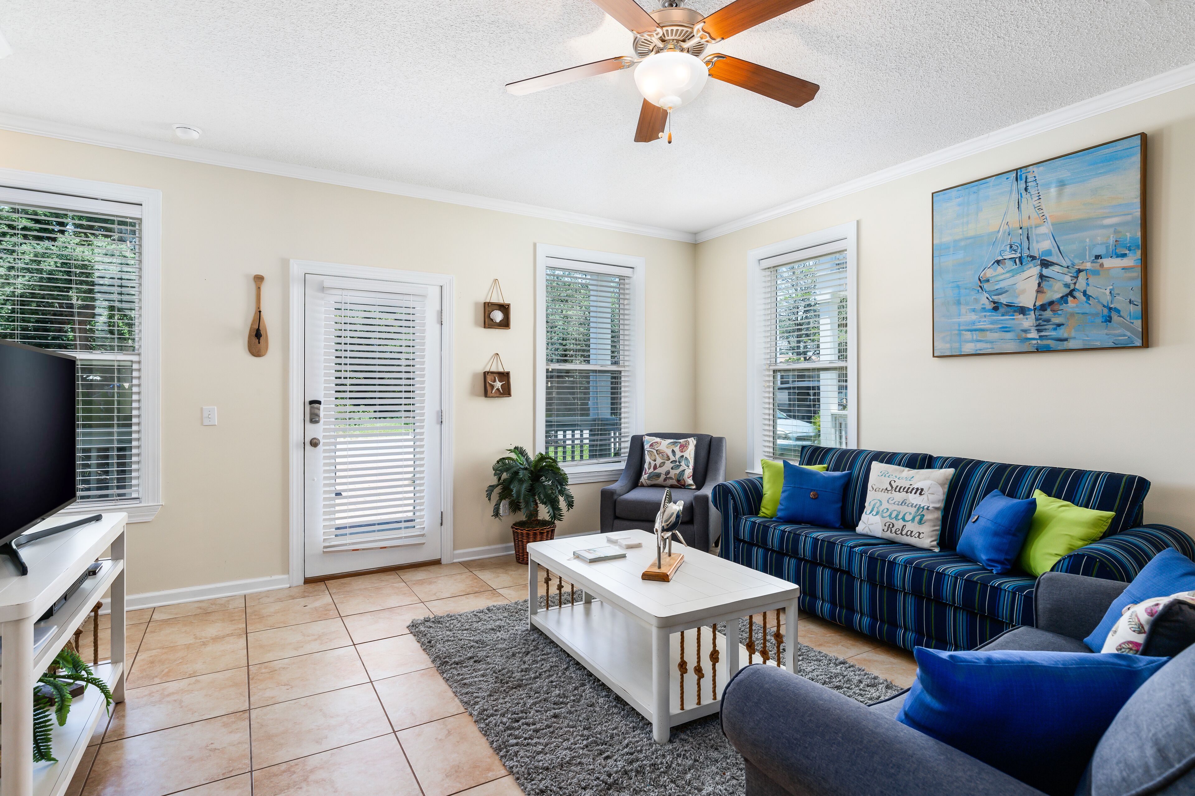 A living room with a ceiling fan, a television on a stand, a striped sofa with cushions, and a painting on the wall.