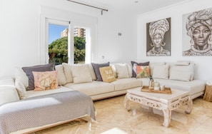 A modern living room with a beige sofa, a patterned ottoman, and a decorative coffee table.