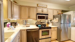 A kitchen with wooden cabinets, stainless steel appliances, a coffee maker, and a kettle. - 30A Beachfront Condo. Steps To The Beach! 3BD,3BA. 25+ Listing (Santa Rosa Beach)