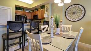 A dining area with a glass table, white chairs, and a chandelier.