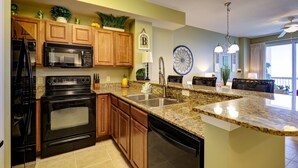 A kitchen with wooden cabinets, a black stove, a microwave, a sink, and a dining area with a ceiling fan.