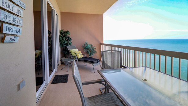 A balcony with a glass door leading to a room, a table, chairs, and a view of the ocean.