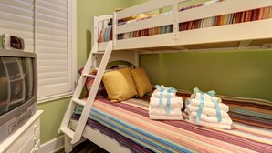 A bunk bed with a TV on a dresser, a window with blinds, and a colorful striped blanket.