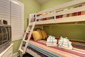 Ein Etagenbett mit Fernseher auf einer Kommode, ein Fenster mit Jalousien und eine bunte, gestreifte Decke.