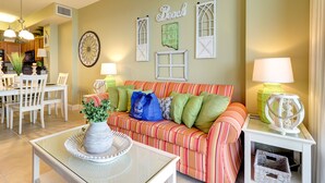 A living room with a striped sofa, a dining table with chairs, a vase with greenery, and wall decorations including a sign that says "Beach".