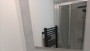 Een badkamer met een wit wastafelmeubel, een spiegel en een douchecabine van glas.