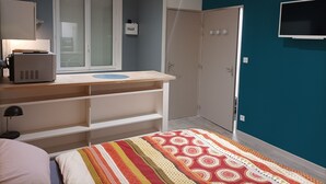 Een slaapkamer met een bed, een bureau met een computer, een kledingkast en een televisie aan de muur.