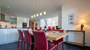 A modern dining area with a wooden table and red chairs, a kitchen in the background, and a wall-mounted lamp. - Ski Paradise SP 011 - MOUNTAIN apartment 6 pers (Veysonnaz)