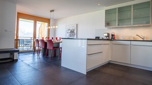 A modern kitchen with white cabinets, a central island, and a dining area with red chairs. - Ski Paradise SP 011 - MOUNTAIN apartment 6 pers (Veysonnaz)