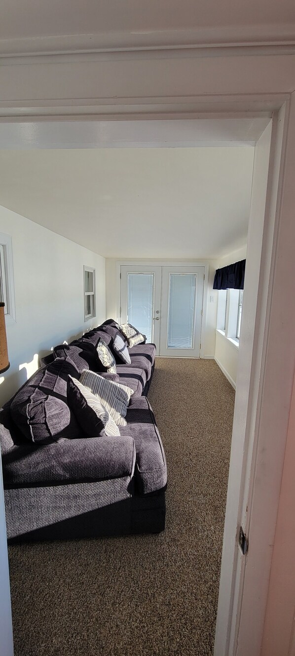 Una habitación con un sofá grande, una puerta y una ventana.