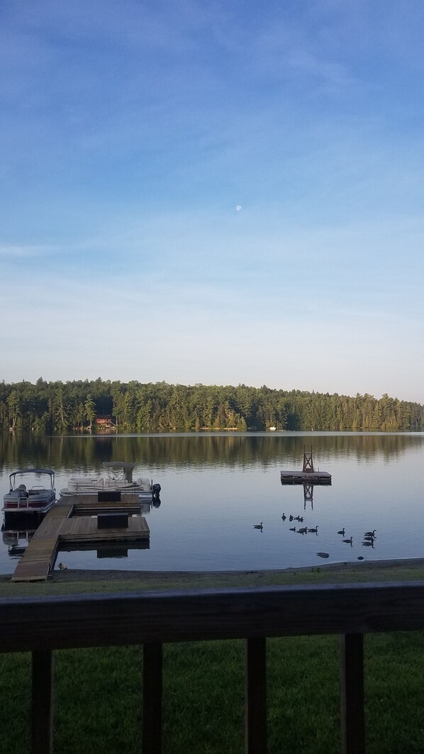 A calm lake with a wooden dock and a house in the background.