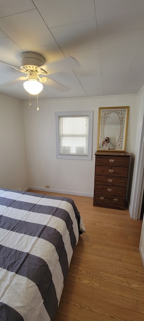 A bedroom with a bed, a dresser, a window, and a ceiling fan.