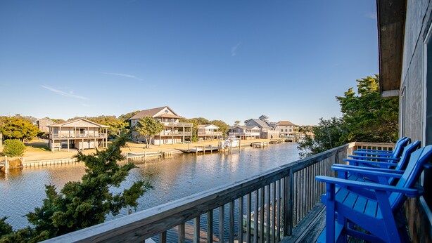 A waterfront property with a wooden deck and blue chairs, overlooking a calm river and residential buildings. - Waterfront, Dog friendly, & private boat ramp (Frisco)
