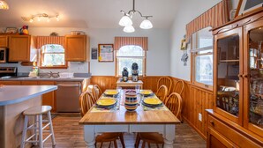 A kitchen with wooden cabinets, a dining table set for four, and a large wooden cabinet with glass doors. - Waterfront, Dog friendly, & private boat ramp (Frisco)