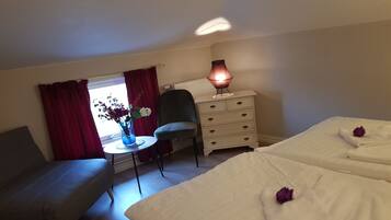 Habitación de hotel con dos camas, una silla, una mesita con un florero y un aparador.