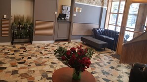 Zona de recepció amb taulell d'entrada, sofà, taula de cafè i un vas amb roses vermelles.