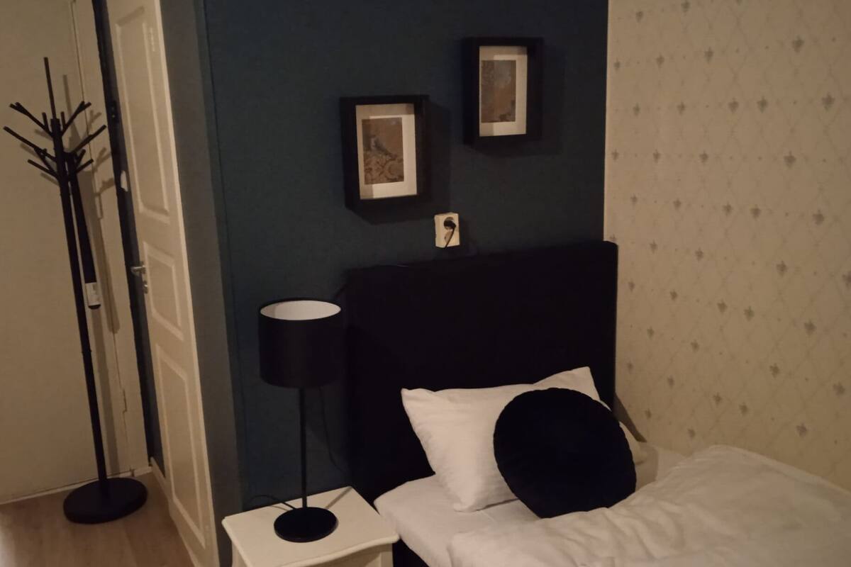 A bedroom with a black headboard, white bedding, a black floor lamp, and two framed pictures on the wall.