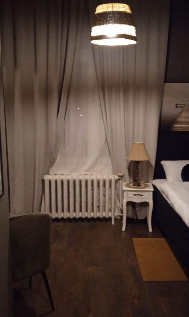 Una habitación de hotel con una cama, una mesita de noche con lámpara, un radiador y una silla.