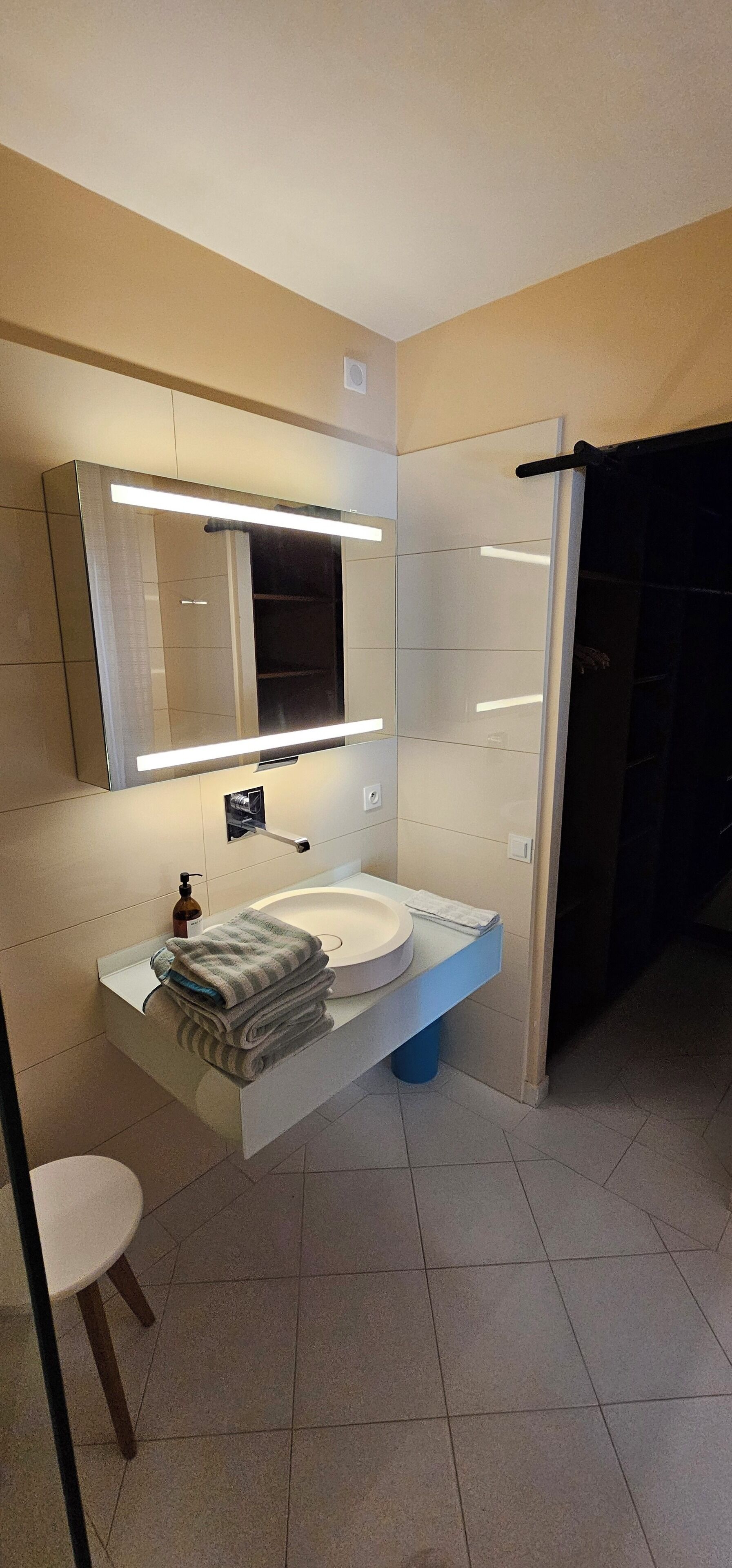 A modern bathroom with a white sink, a mirror with integrated lighting, and a towel rack.
