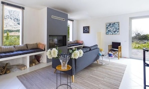 Un salon moderne avec un canapé, une table basse et une cheminée. Il y a une fenêtre donnant sur une montagne et un balcon.