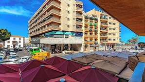 A multi-story hotel with balconies, a ground-level restaurant, and a parking area with cars and buses. - Home2Book Central Studio near Playa del Muelle (Puerto de la Cruz)