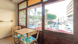 A room with a wooden table and chairs, large windows with a view of a parking lot and palm trees. - Home2Book Central Studio near Playa del Muelle (Puerto de la Cruz)