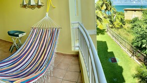 A balcony with a hammock, a small table, and a view of the ocean and greenery. - Beachfront Paradise Resort Villa near San Juan (Rio Grande)