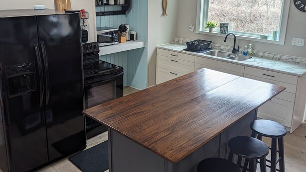 Una cocina moderna con un refrigerador negro, una isla de madera y taburetes de bar.