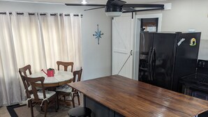 Una cocina compacta con una isla central, taburetes de bar, una mesa de comedor con sillas, un refrigerador y un ventilador de techo.