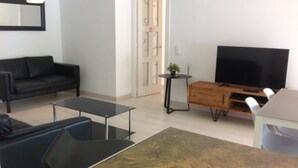 A modern living room with a black sofa, a glass coffee table, a wooden TV stand, and a flat-screen TV. - APT 3 BEDROOMS TERRACE SEA VIEW BEACH ROSAS - NEW AIR CONDITIONING- PRIVATE PARKING (Roses ( petites Canyelles ))