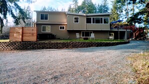 A two-story house with a gravel driveway and a wooden fence. - Mid-Century Modern House w/Tiki Room & Hot Tub (Bonney Lake)