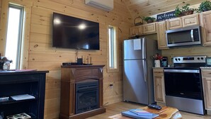 A wooden cabin interior with a flat-screen TV, a built-in fireplace, a stainless steel refrigerator, a microwave, and a stove.