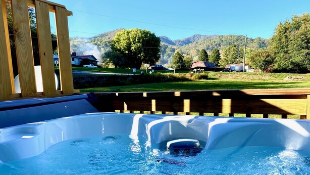 A hot tub with a wooden deck and a view of a rural landscape with houses and mountains.