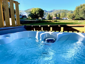A hot tub with a wooden deck and a view of a rural landscape with houses and mountains.