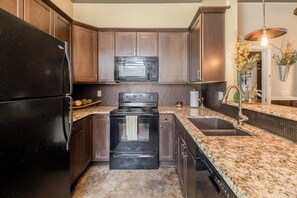 Una cocina moderna con armarios de madera oscura, un refrigerador negro, un microondas, una estufa y una encimera de granito.