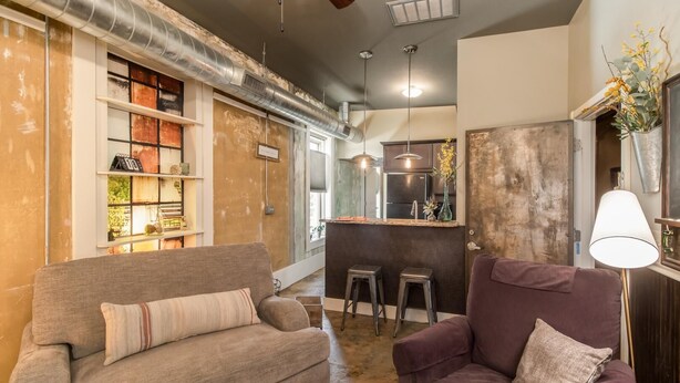 Een moderne woonkamer met een bank, een paarse fauteuil en een keukenhoek met krukken.