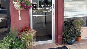 Het uiterlijk van Antler Lofts Apartments, met een rode bakstenen gevel, een groen luifel en een deur met een welkomstmat.