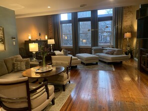 A spacious living room with a wooden floor, a large window, and a fireplace.