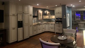 A modern kitchen with white cabinetry, a dining area with a round table, and a view of the city through a window. - Historic Loft Main st. in the Heart of Downtown Greenville (Greenville)