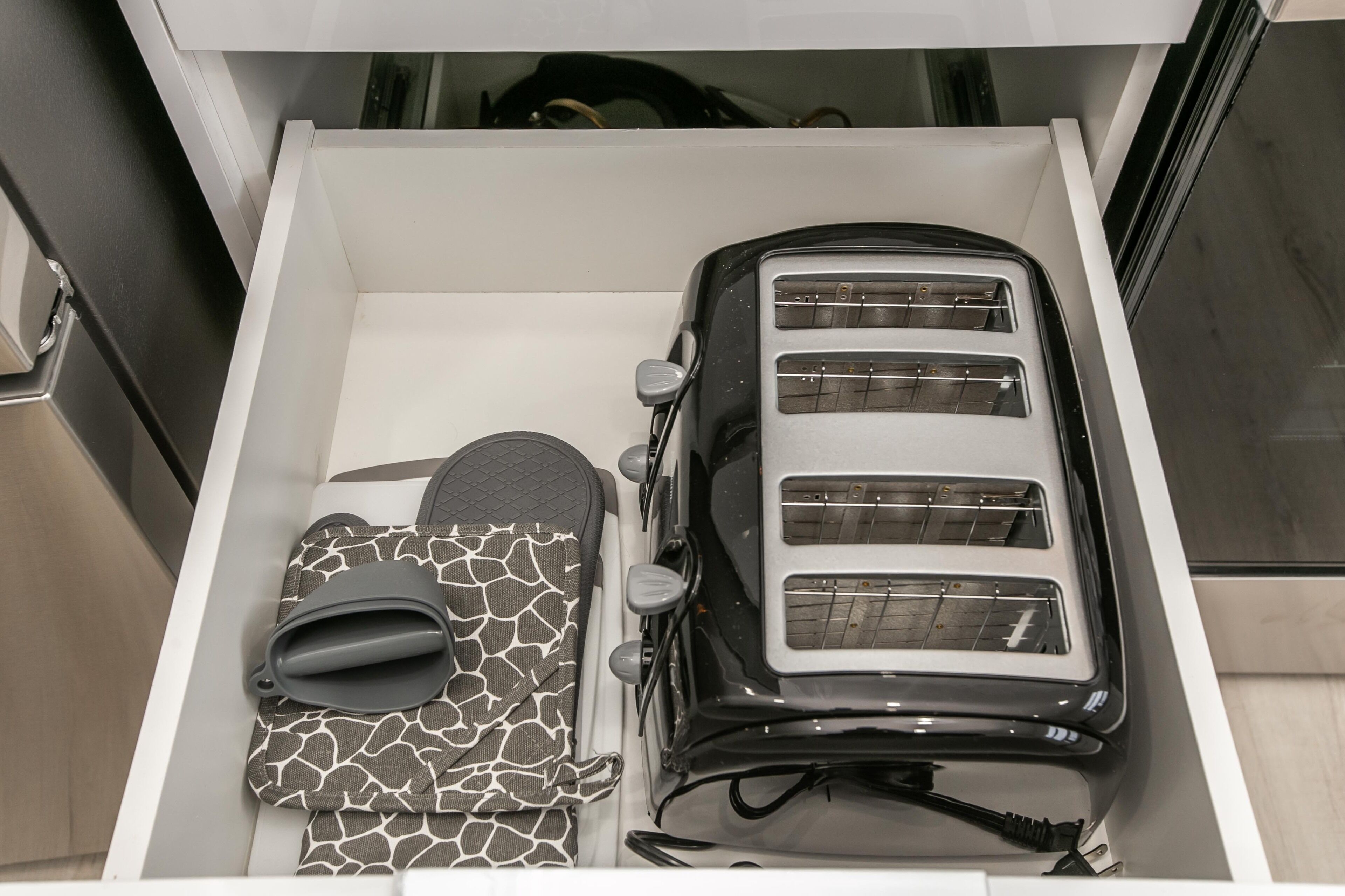 Eine Schublade mit einem Toaster, Hausschuhen und einer gemusterten Tasche.