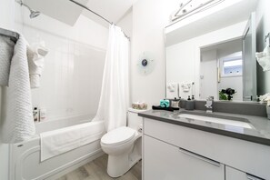A modern bathroom with a bathtub, toilet, and a large mirror. - ☆NEW☆Chic Modern 3BDRM☆Central☆WiFi☆Netflix✔Clean! (Edmonton)