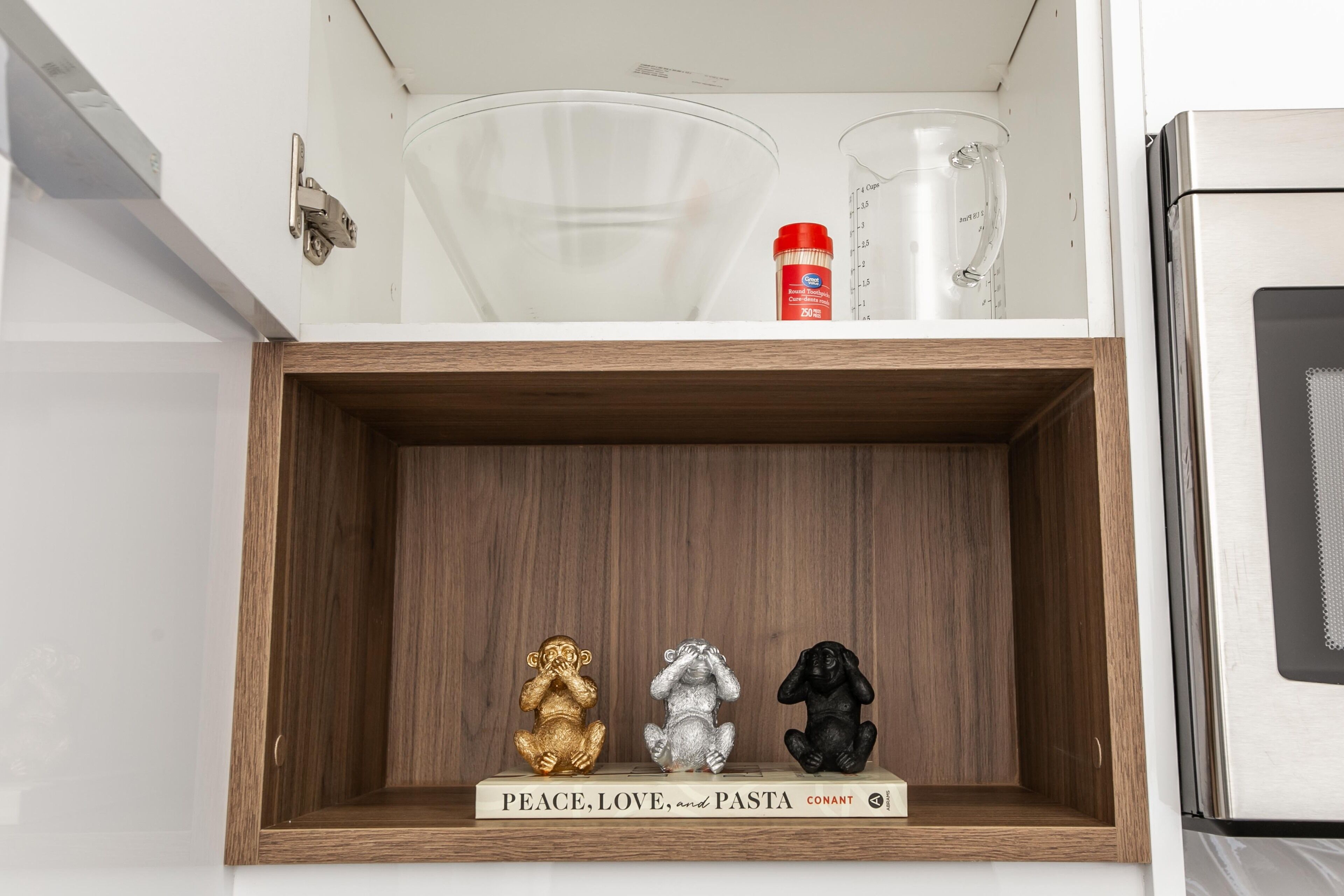 Uno scaffale da cucina con un libro intitolato 'PEACE, LOVE, and PASTA' e tre figurine a forma di scimmia.